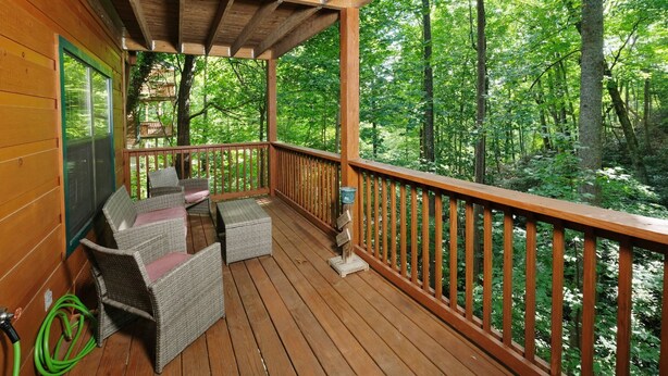 Una terraza de madera con mobiliario de mimbre y vistas a un bosque.