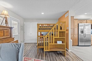 A room with a bunk bed, a wooden dresser, a refrigerator, and a door with a window. - Lazy Days M-01A - Three Bedroom House, Sleeps 10 (Osage Beach)