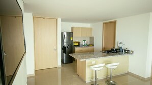Una cucina moderna con frigorifero in acciaio inossidabile, forno integrato e piano di lavoro in granito. Sono presenti due sgabelli da bar bianchi e un'isola con lavello.