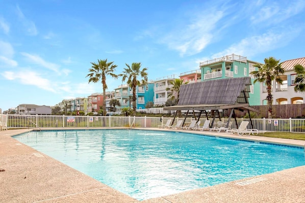 A swimming pool with a wooden deck and lounge chairs, surrounded by a white fence.