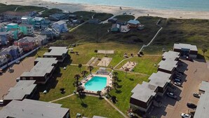 Vista aérea de una zona residencial costera con piscina, rodeada de casas y una playa al fondo.