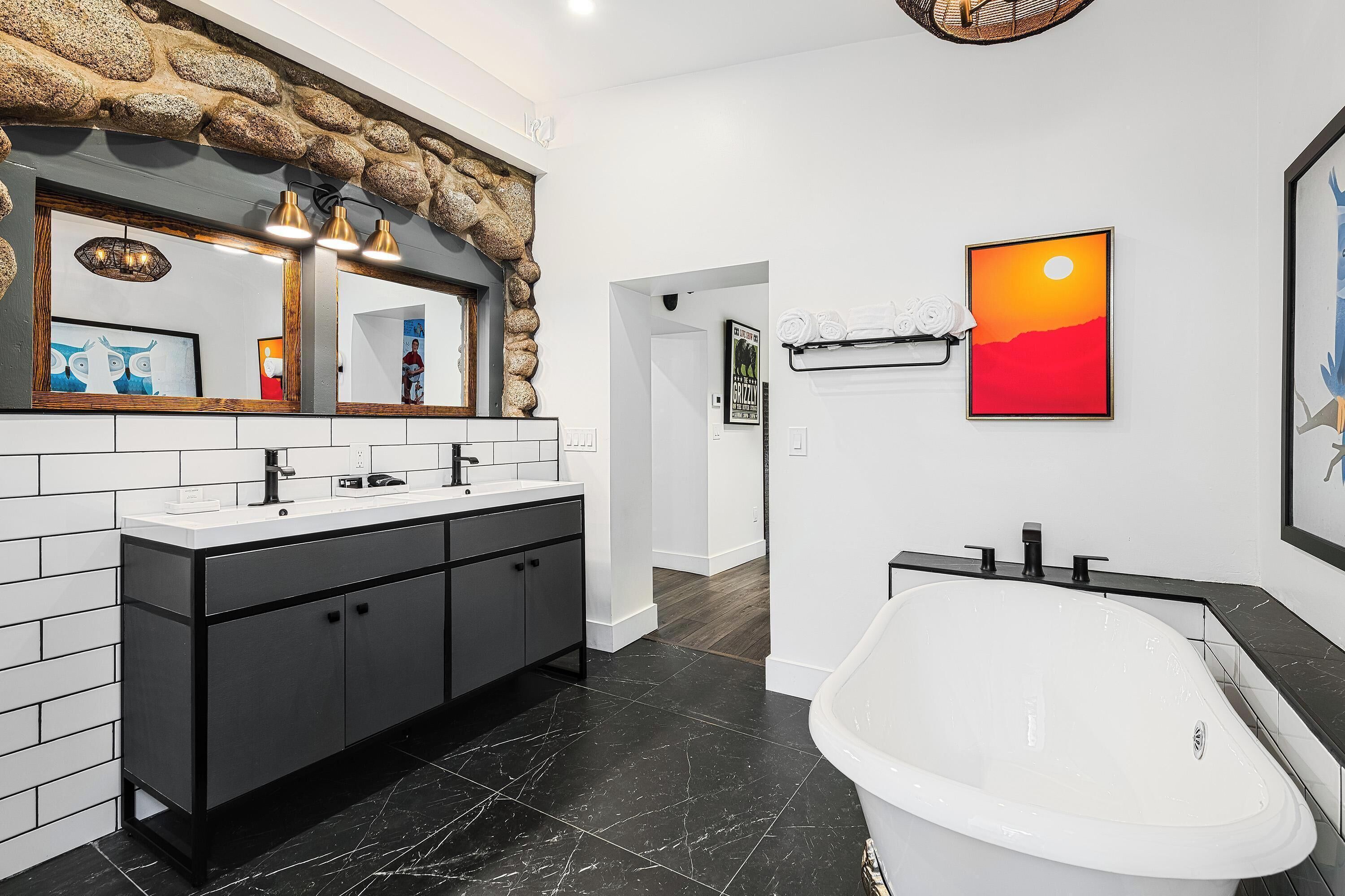 A modern bathroom with a large bathtub, a double sink vanity, and a stone accent wall.