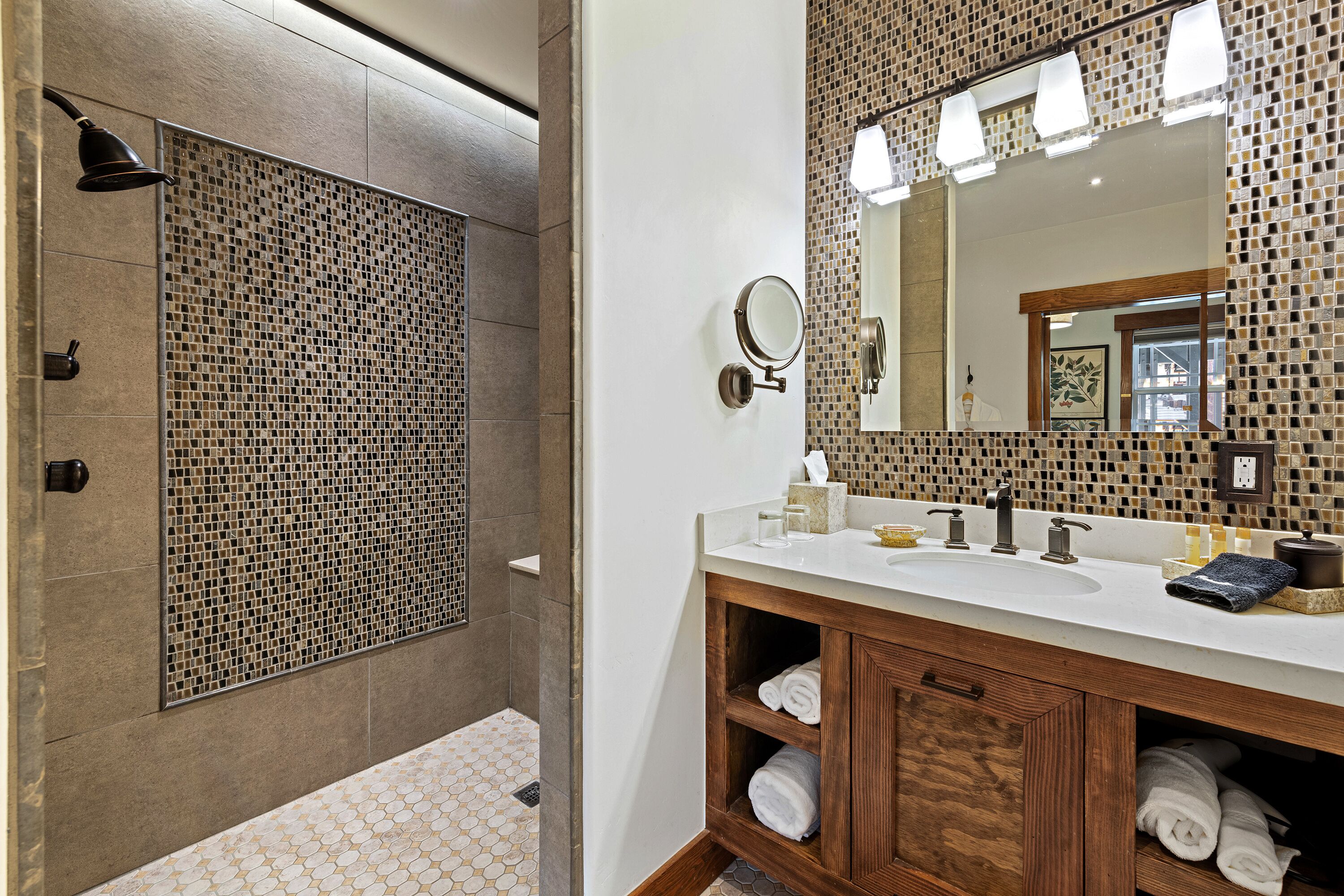 A bathroom with a shower, a sink with a mirror, and a wooden vanity with towels.