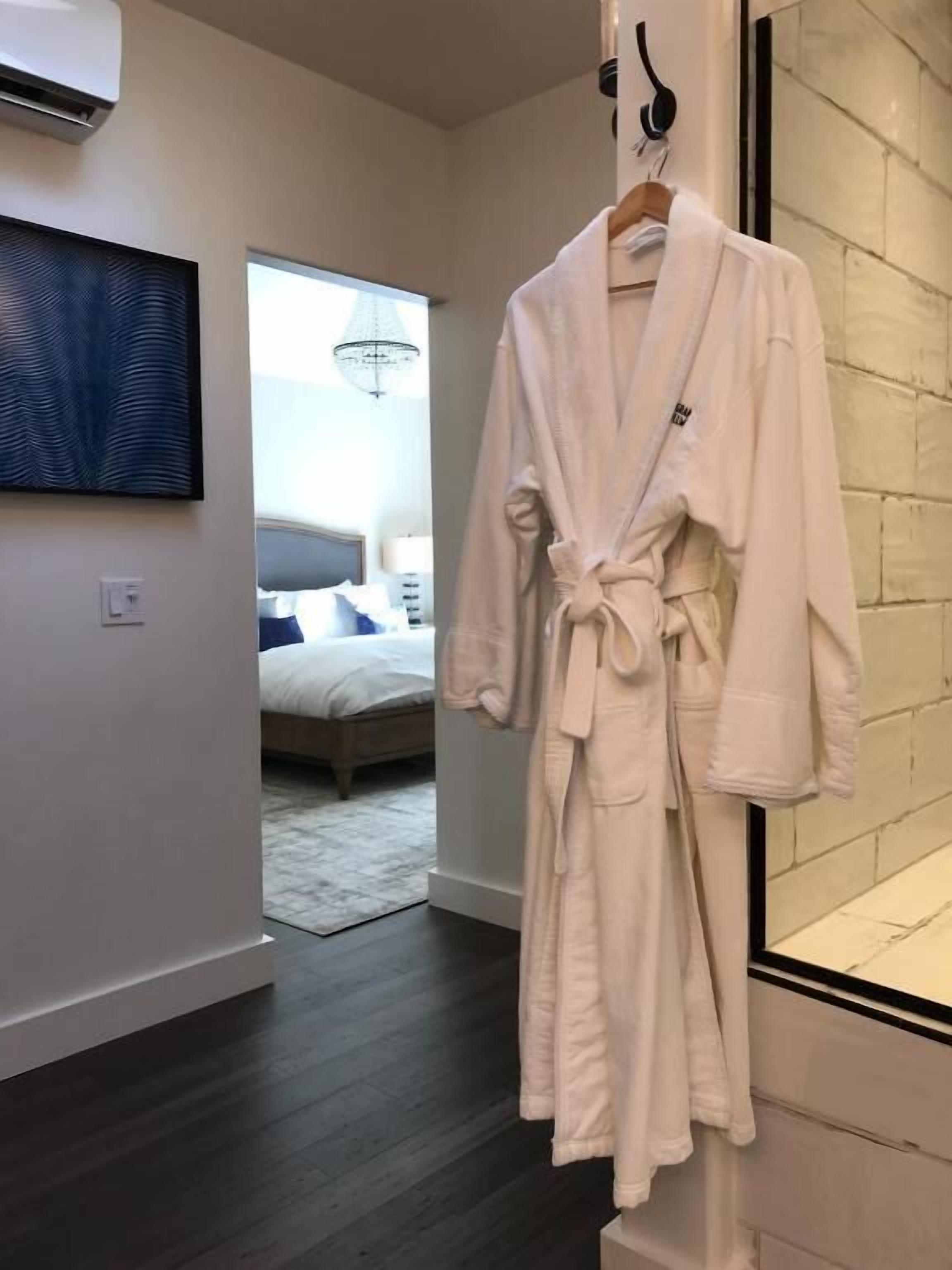 A white bathrobe hanging on a hook in a modern bathroom with a large mirror and a painting on the wall.