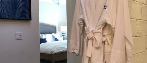 A white bathrobe hanging on a hook in a modern bathroom with a large mirror and a painting on the wall.