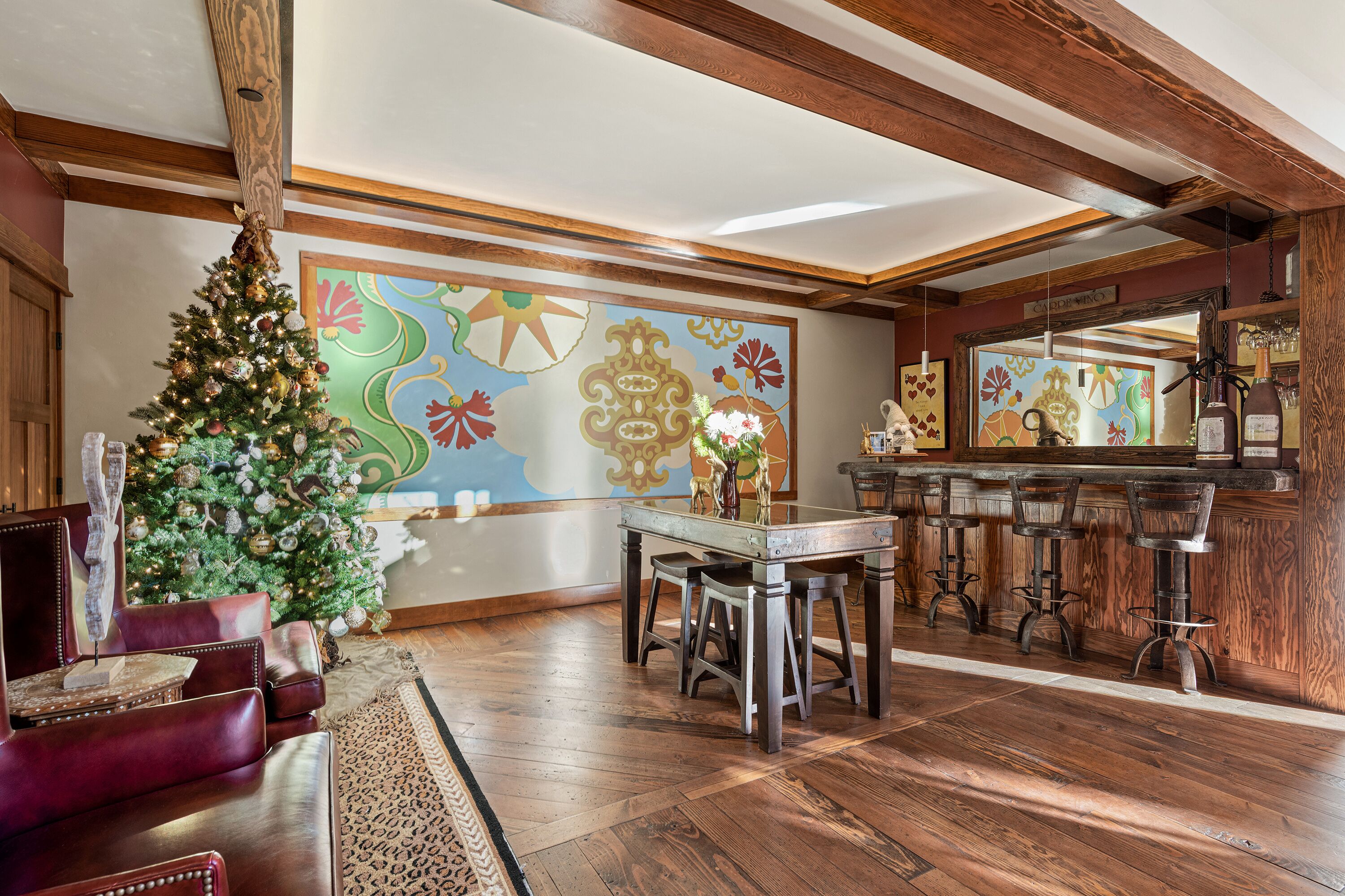 Een gezellige woonkamer met een houten plafond, een kerstboom, een groot abstract schilderij en een bar met krukken.