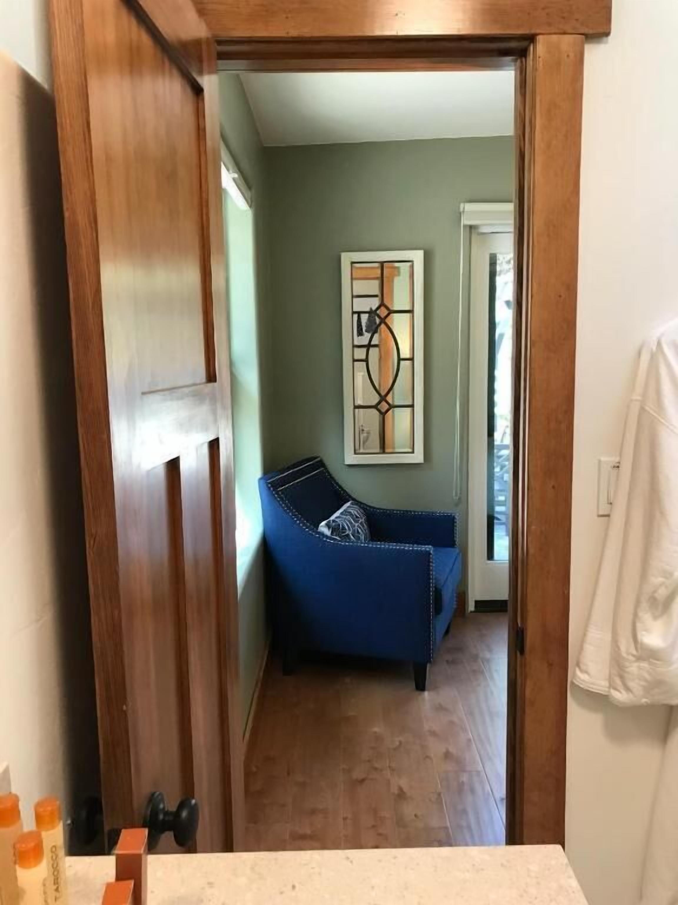 A hallway leading to a room with a blue sofa, a framed artwork on the wall, and a wooden door frame.