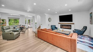 A spacious living room with a sectional sofa, a flat-screen TV mounted on the wall, and a fireplace. - Zion Luxe Family Escape: HotTub, Games, Sleeps 14 (Glendale)