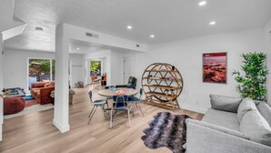 A spacious living area with a round dining table, a grey sofa, and a large bookshelf. - Zion Luxe Family Escape: HotTub, Games, Sleeps 14 (Glendale)