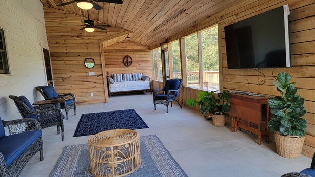 Een houten chalet met een plafondventilator, een bank, rieten stoelen, een televisie en potplanten.