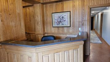 A reception area with a wooden reception desk, a framed artwork on the wall, and a hallway leading to other rooms.