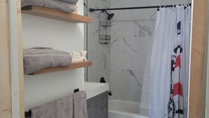 A bathroom with a bathtub, toilet, and a shower curtain. There are towels on a shelf and a shower head mounted on the wall. - Central to Everything ...Cedar Point, Downtown and Sports Park.   (Sandusky)