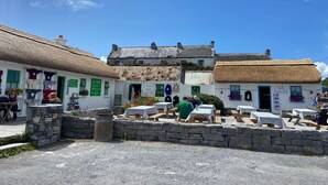 A traditional building with a thatched roof, stone walls, and outdoor seating area with tables and benches. - (Family and pet friendly), Inishmore, Aran Islands, Large spacious property! (Creig a'Chéirin)