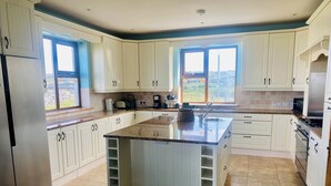 A spacious kitchen with white cabinets, a central island, and a large window providing a view of the outdoors. - (Family and pet friendly), Inishmore, Aran Islands, Large spacious property! (Creig a'Chéirin)