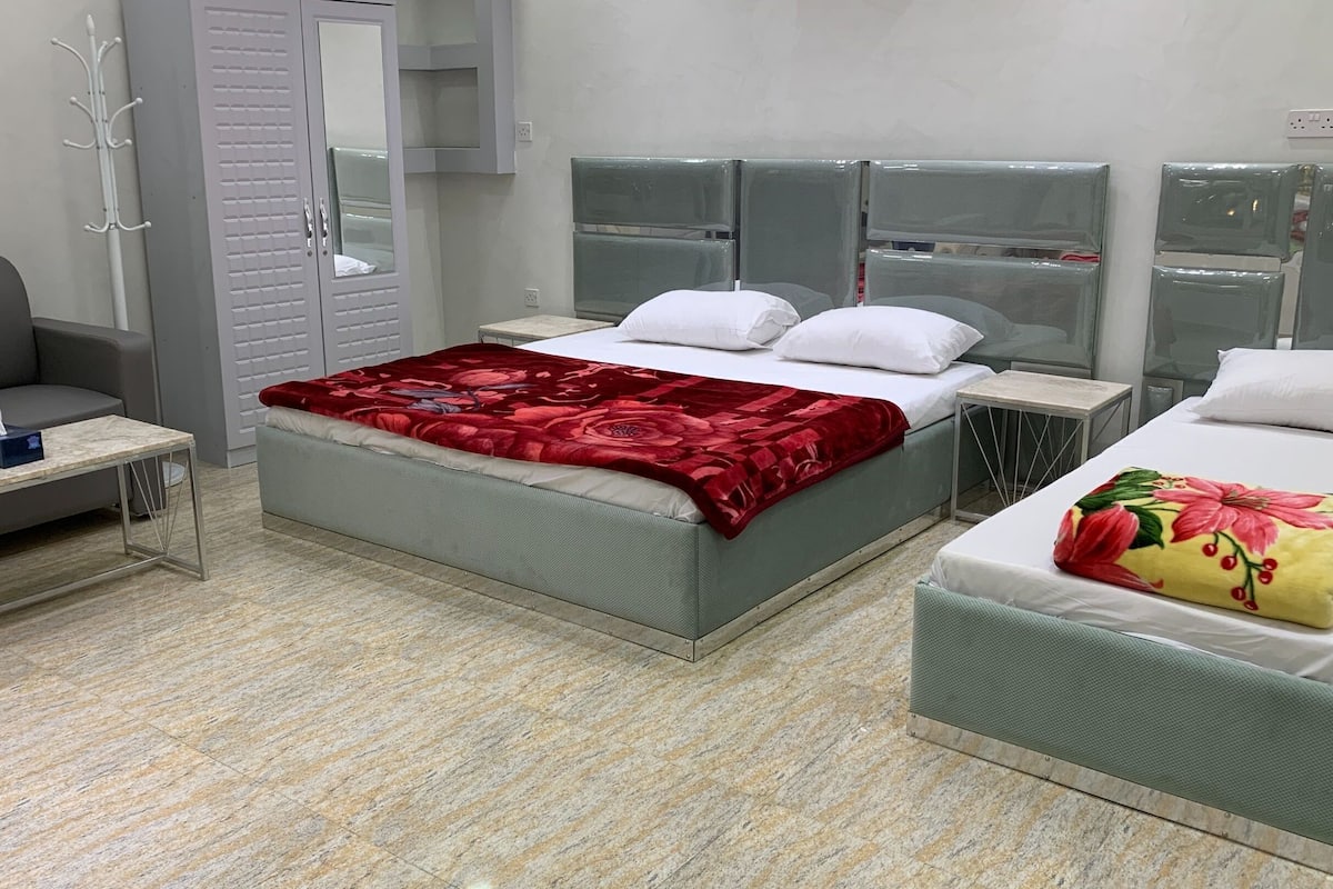 A hotel room with a bed, a sofa, a small table, and a mirror.