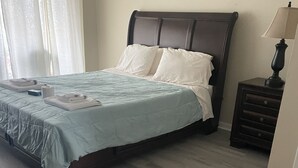 A neatly made bed with a light blue bedspread and white pillows, a wooden floor, and a small bedside table with a lamp. - El Palacio de la Pesca (Lake Placid)