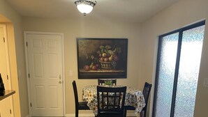 A dining area with a table set for four, a painting above the table, and a sliding glass door to the right. - El Palacio de la Pesca (Lake Placid)