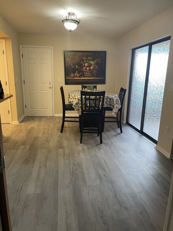 A dining area with a table set for four, a painting above the table, and a sliding glass door to the right.