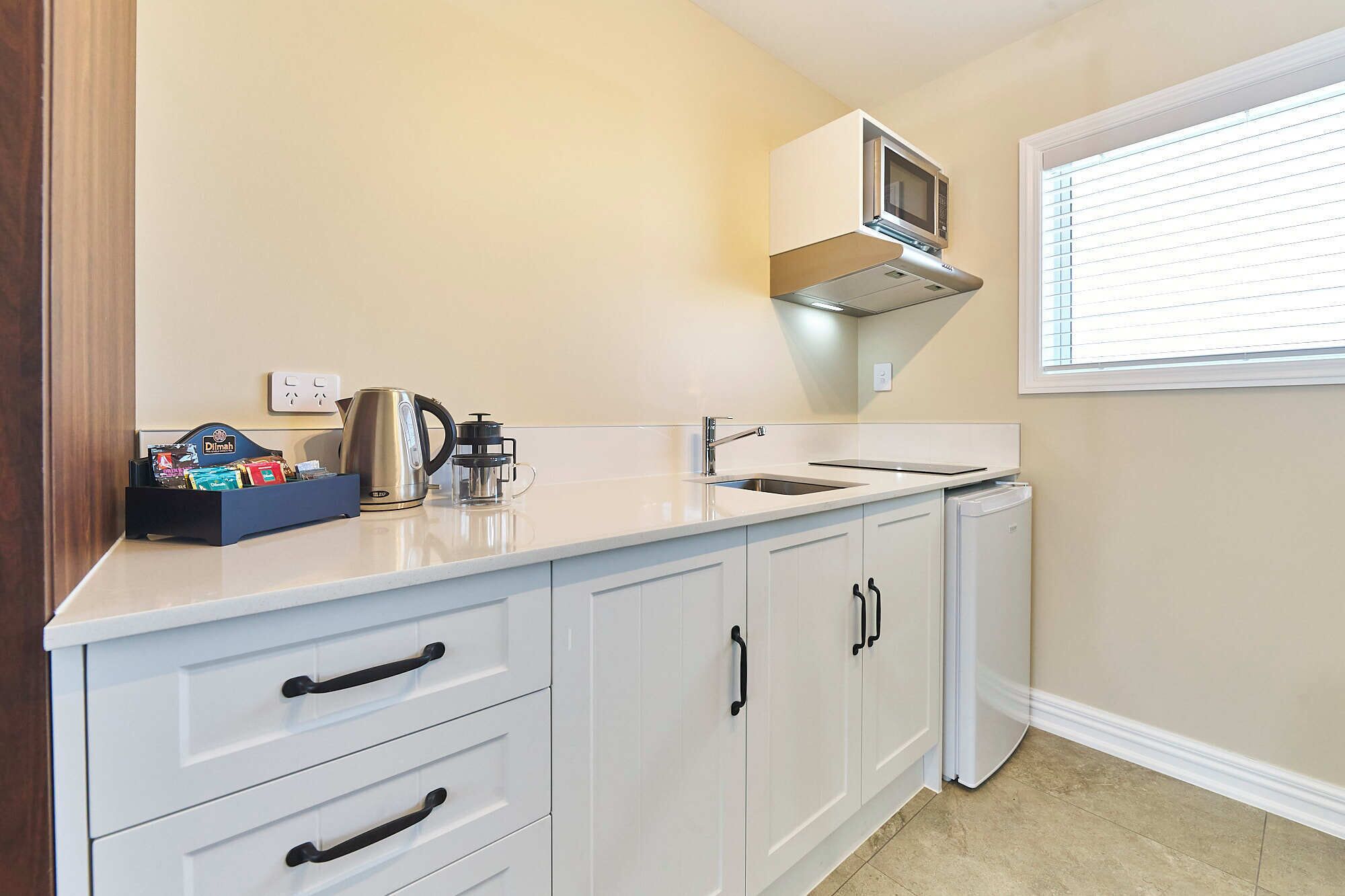 A kitchen with white cabinets, a microwave, a kettle, and a coffee maker.