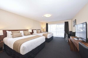 A hotel room with two beds, a desk with a computer, and a large window.