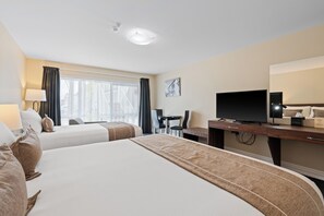 A hotel room with two beds, a desk, a television, and a window with curtains.