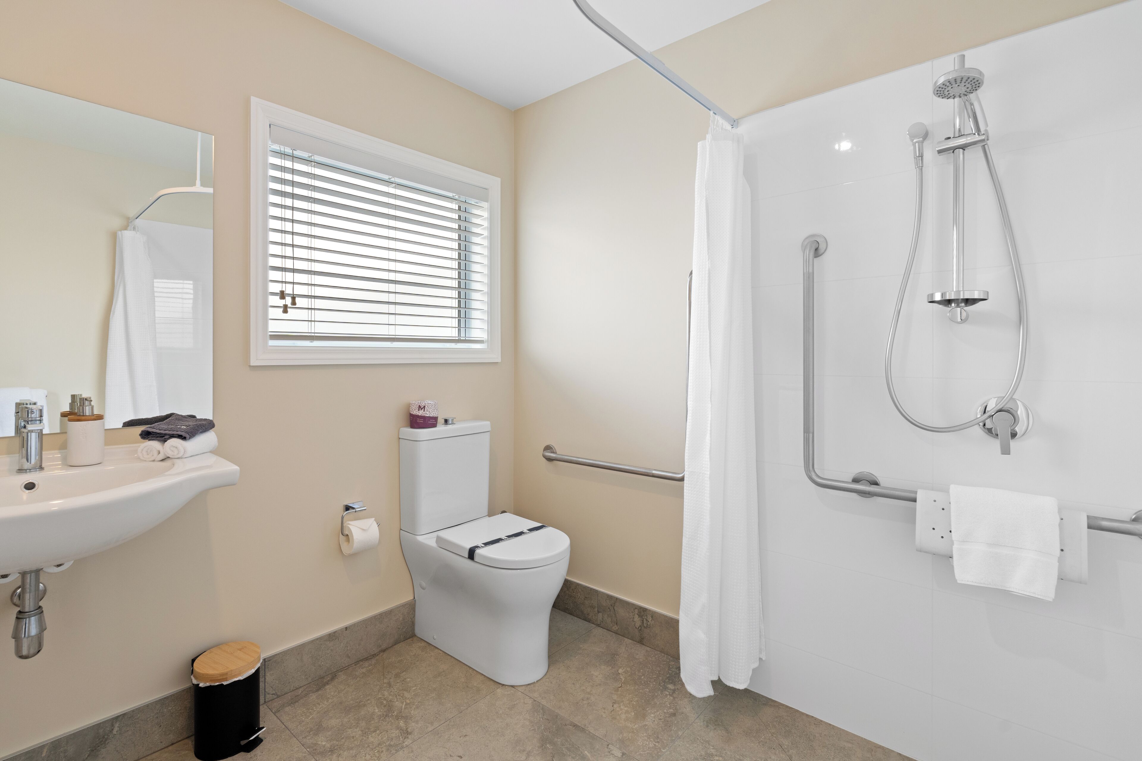 Een moderne badkamer met een wastafel, toilet, douche en een raam met zonwering.