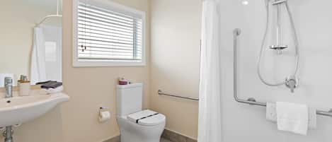 A modern bathroom with a sink, toilet, shower, and a window with blinds.