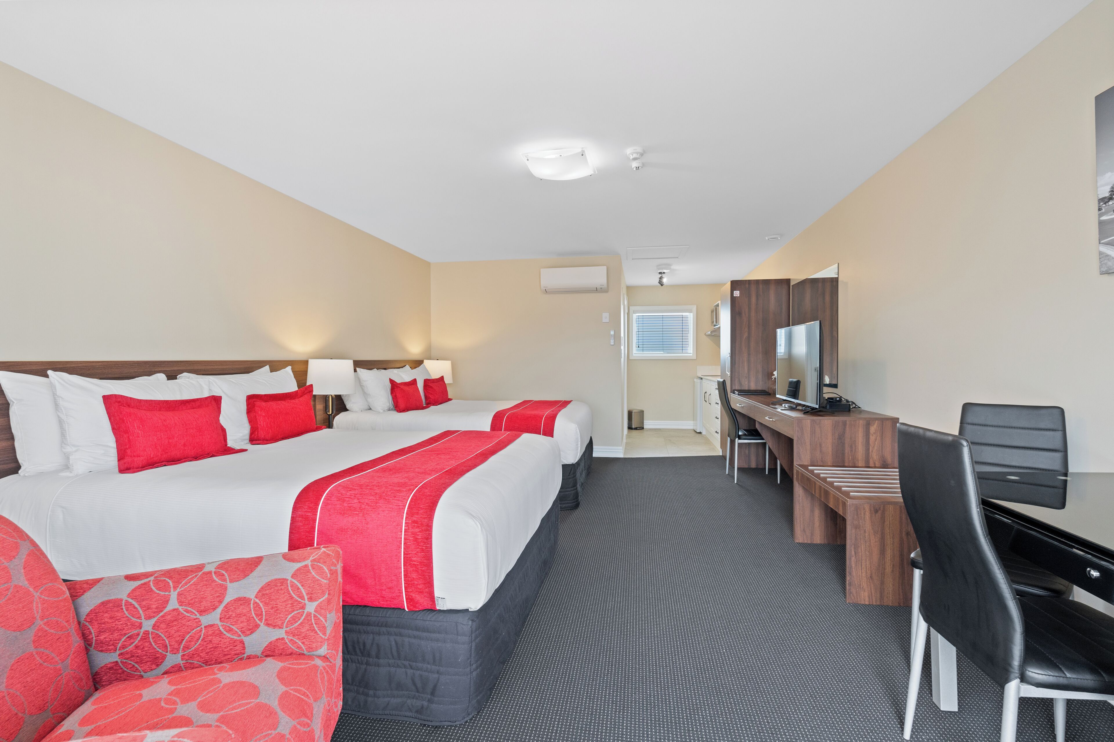 A hotel room with two beds, a desk, a chair, a TV, and a window.