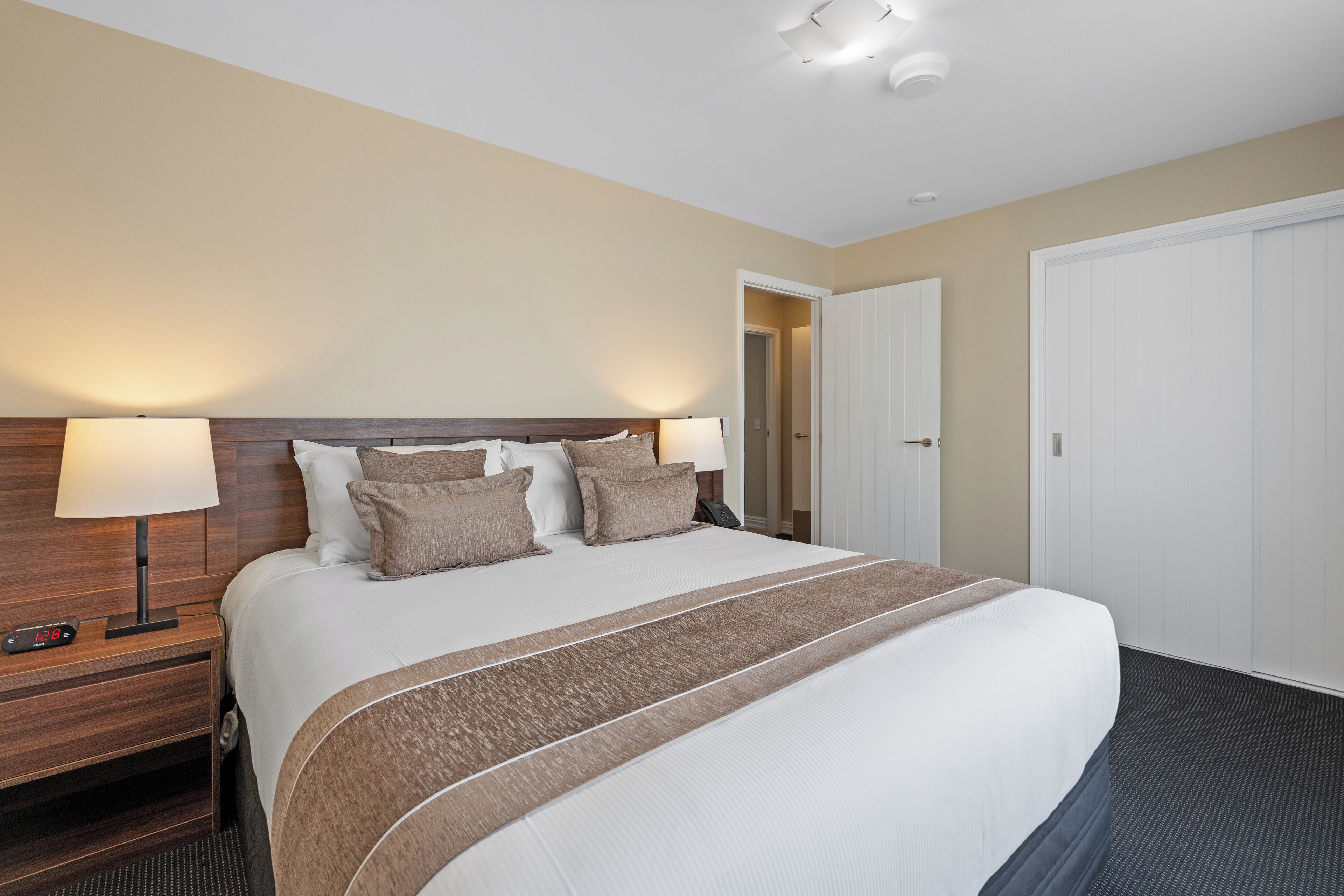 A hotel room with a large bed, two bedside lamps, a wooden nightstand, and a door to another room.
