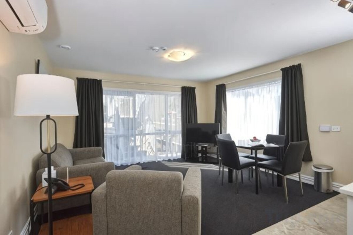 Habitación de hotel con sofá, una mesa de comedor con sillas, televisor y lámpara.