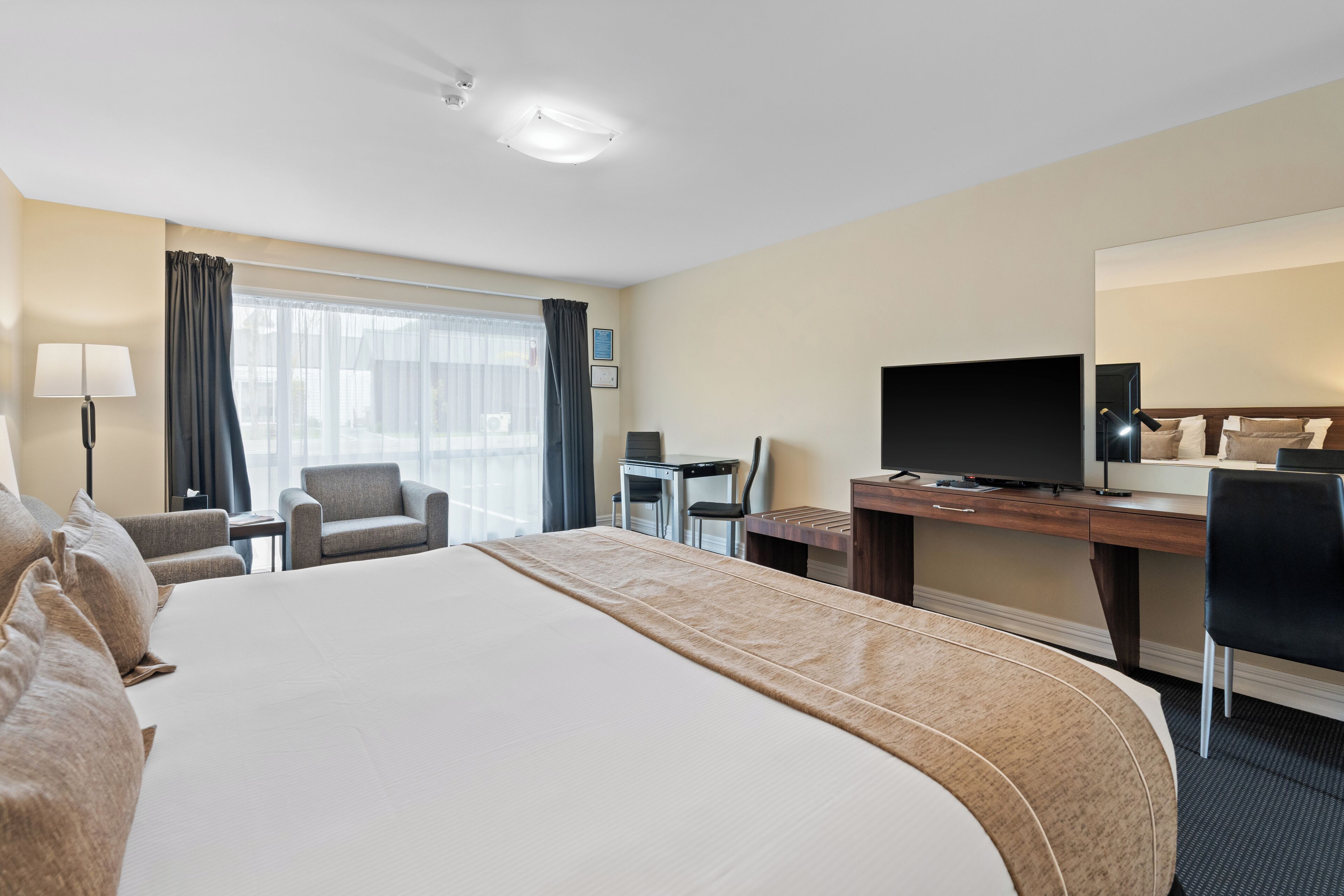 A hotel room with a large bed, a desk with a computer, a TV, and a chair.