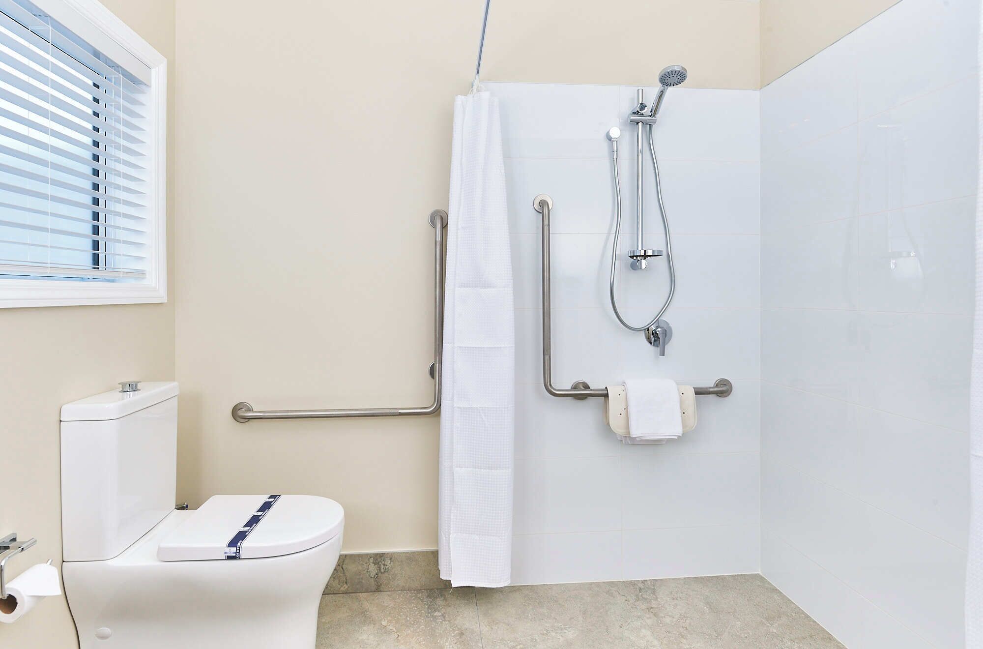 A bathroom with a toilet, a shower with a handheld showerhead, grab bars, and a towel rack.