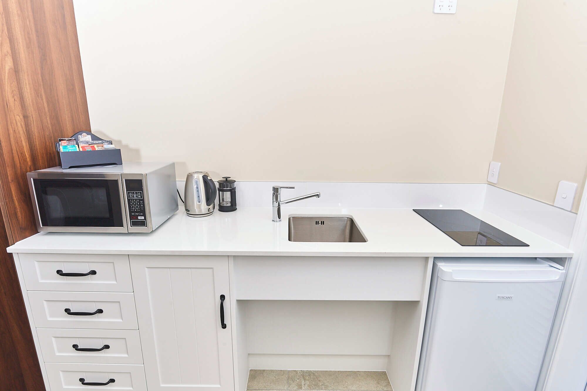 A compact kitchenette with a microwave, kettle, coffee maker, sink, and a small refrigerator.