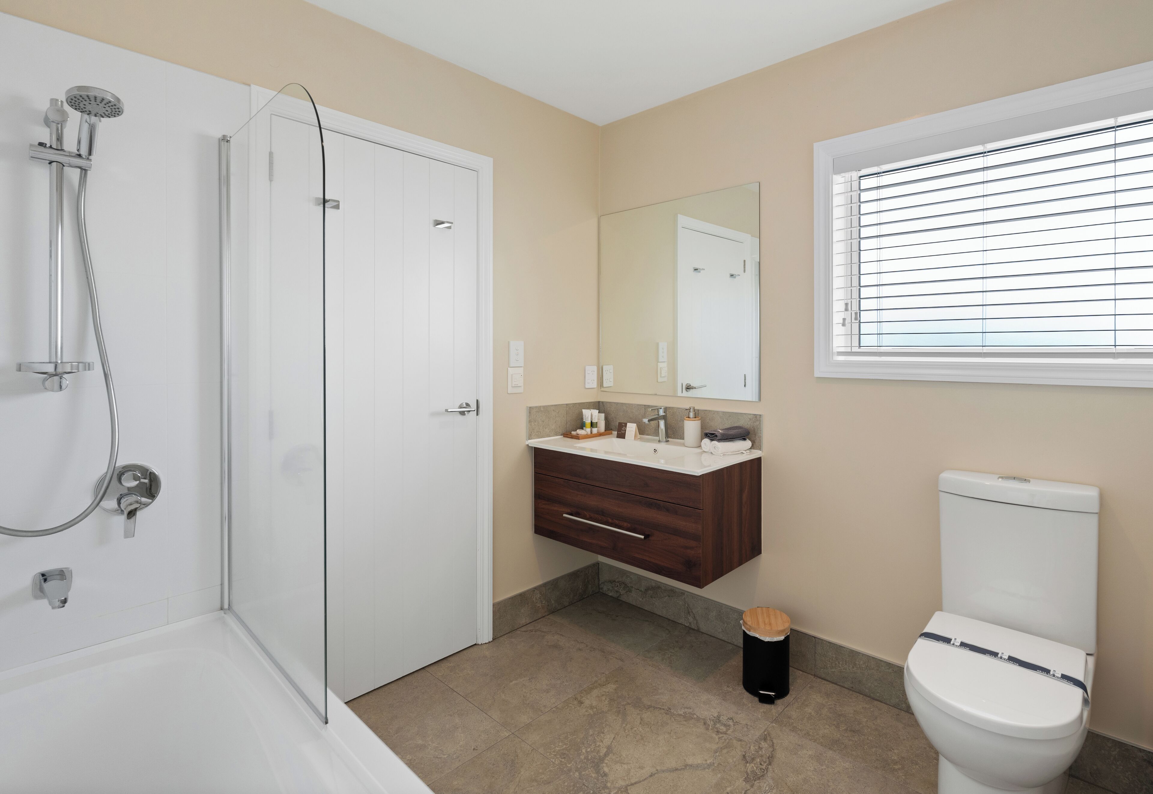 Une salle de bain équipée d’une douche, de toilettes, d’un lavabo et d’une fenêtre avec des stores.