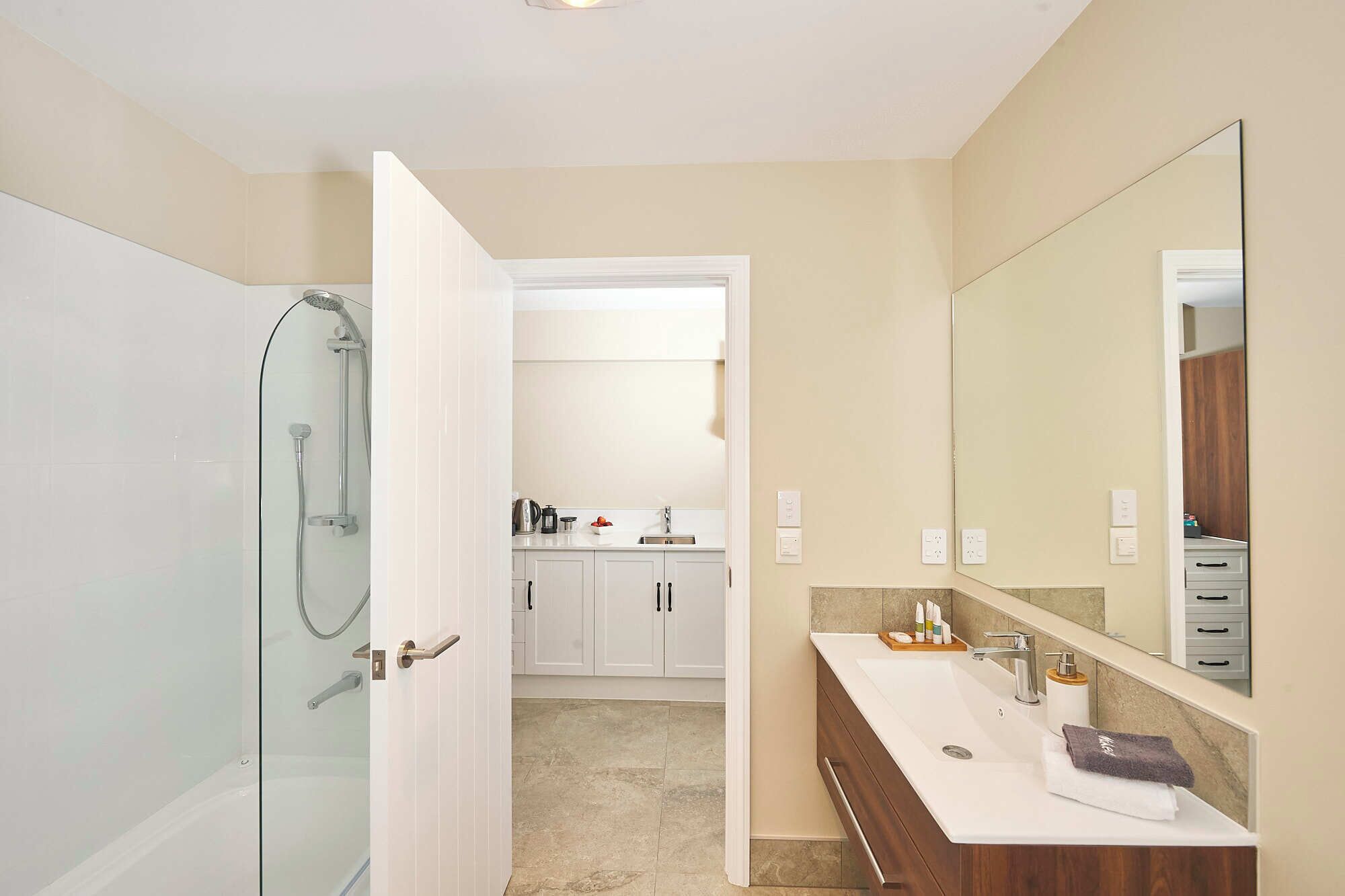 A bathroom with a glass shower enclosure, a white sink with a wooden vanity, and a large mirror.