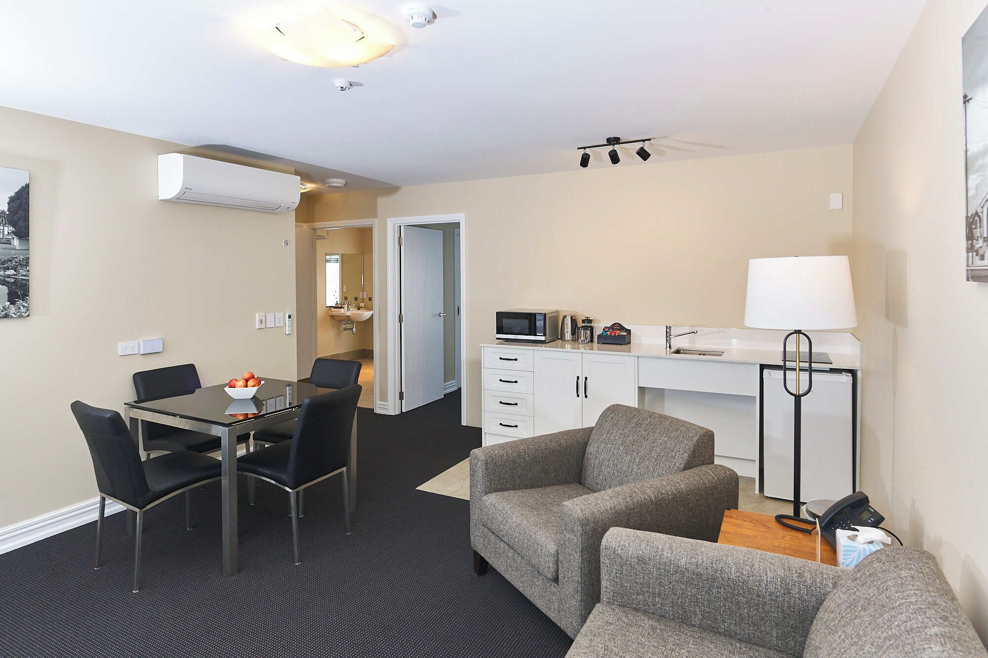 A modern hotel room with a dining area, kitchenette, and seating space.