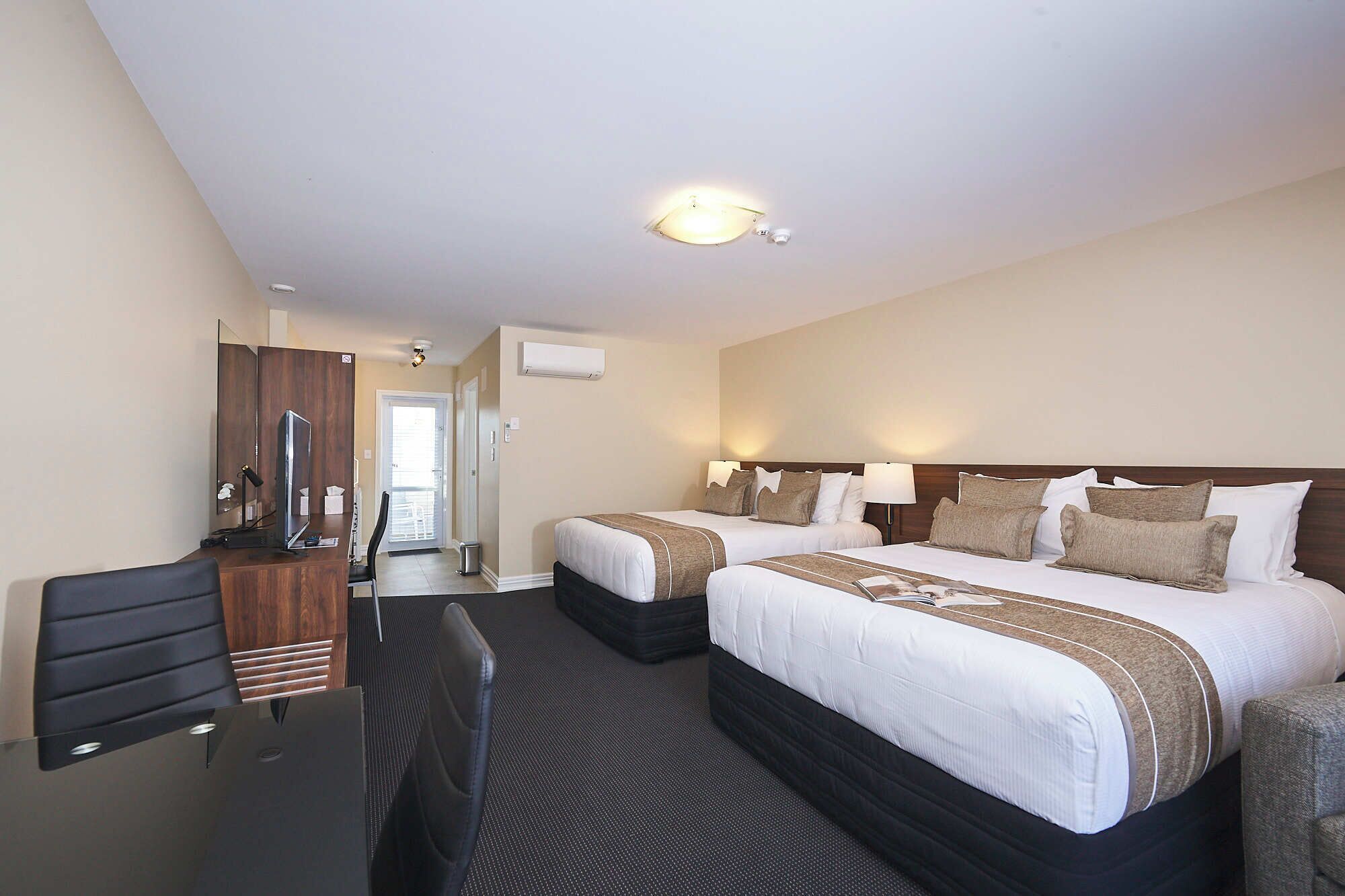 A hotel room with two beds, a desk with a chair, a mirror, and a ceiling light.