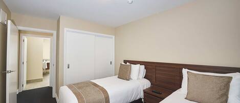 Habitación de hotel con dos camas, un armario, un baño a la vista a través de una puerta abierta y una lámpara en el techo.