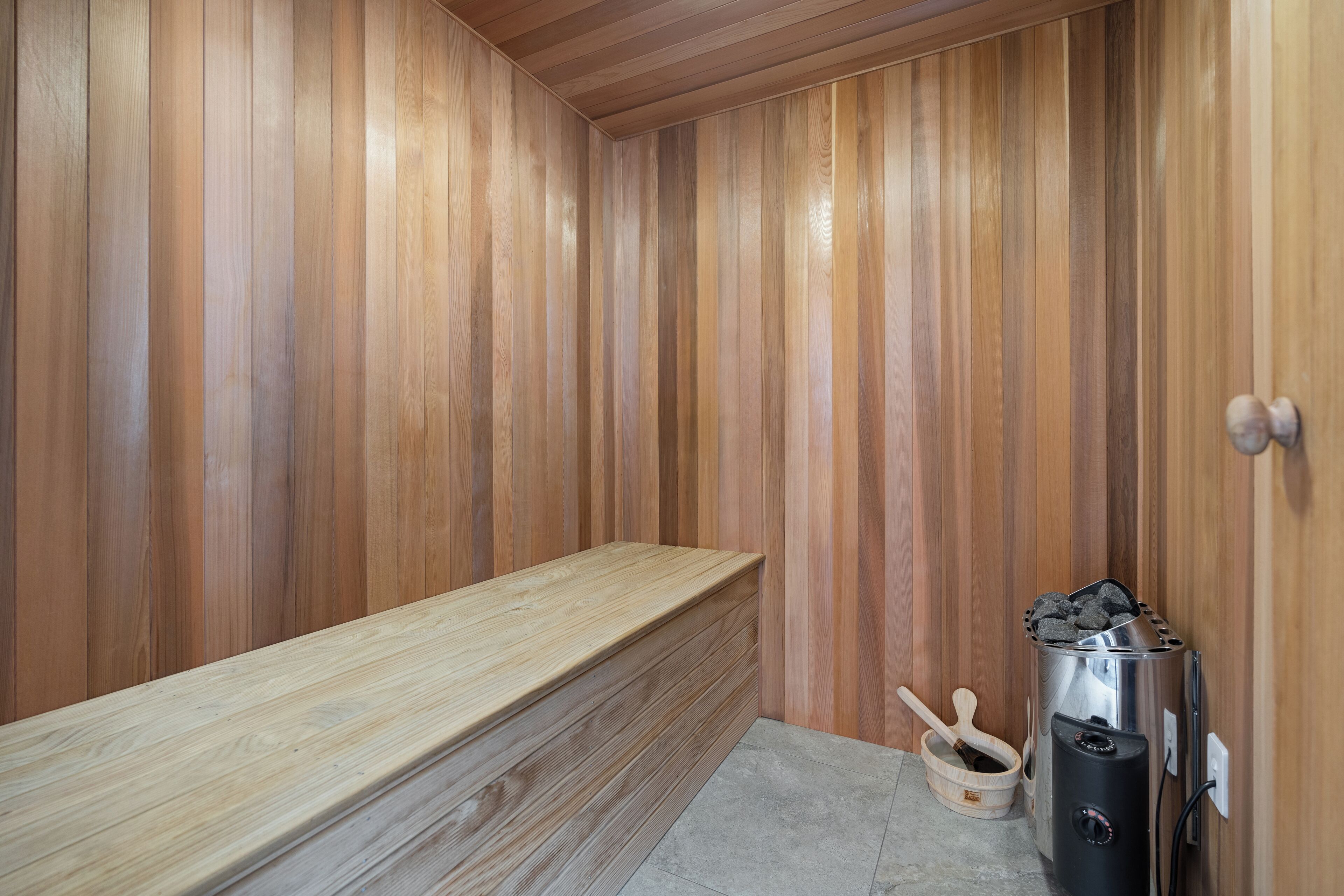 A sauna with wooden walls, a bench, a charcoal stove, and a wooden scoop.
