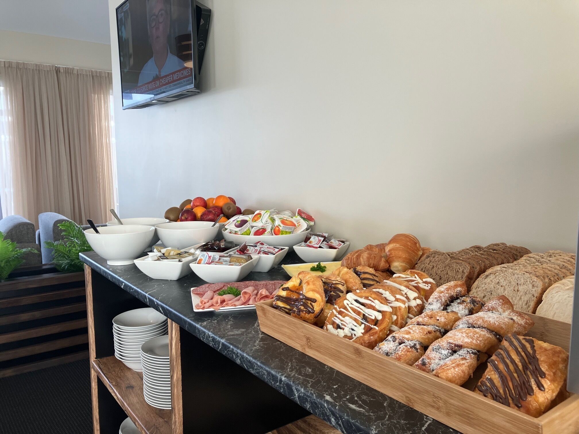A buffet table with various food items including fruits, pastries, and deli meats.