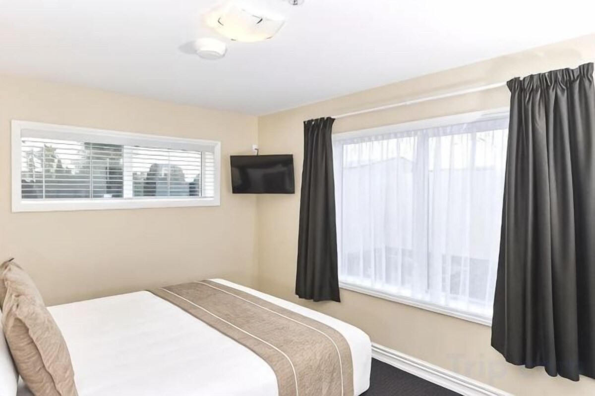 Una camera d'albergo con un letto, una televisione a parete e una finestra con tende.