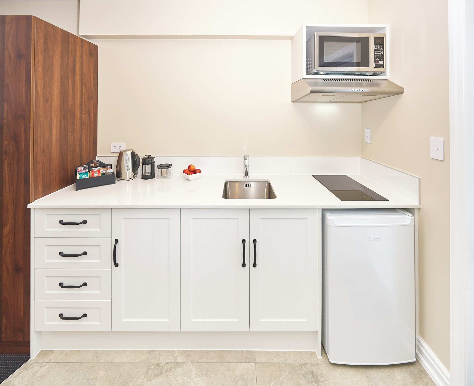 A compact kitchen with white cabinetry, a stainless steel sink, a microwave, and a built-in dishwasher.