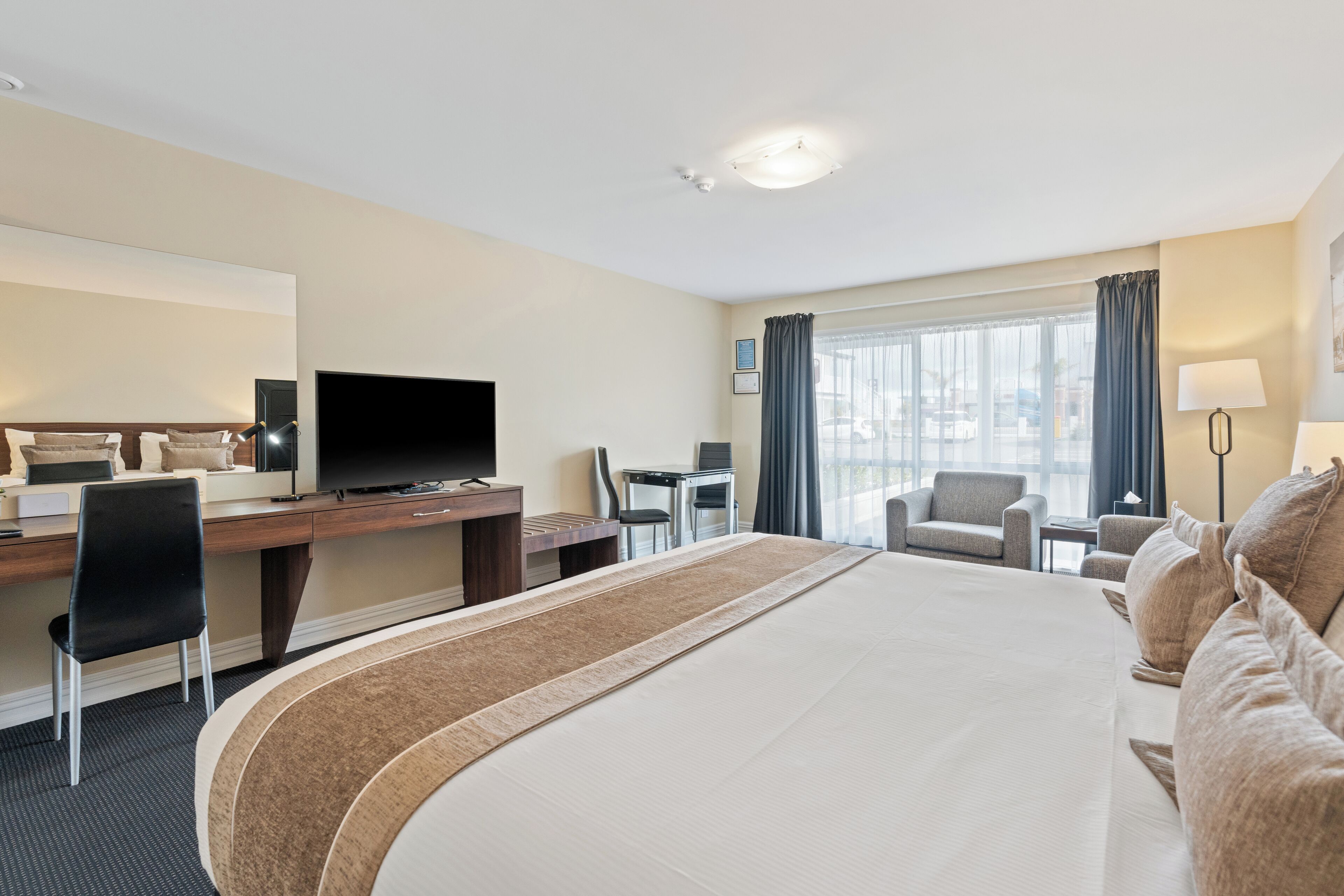 Habitación de hotel con una cama grande, un escritorio con televisor, una silla y vista a la ciudad desde la ventana.