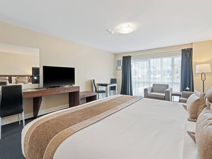 Ein Hotelzimmer mit einem großen Bett, einem Schreibtisch mit Fernseher, einem Sessel und Blick auf die Stadt durch das Fenster.