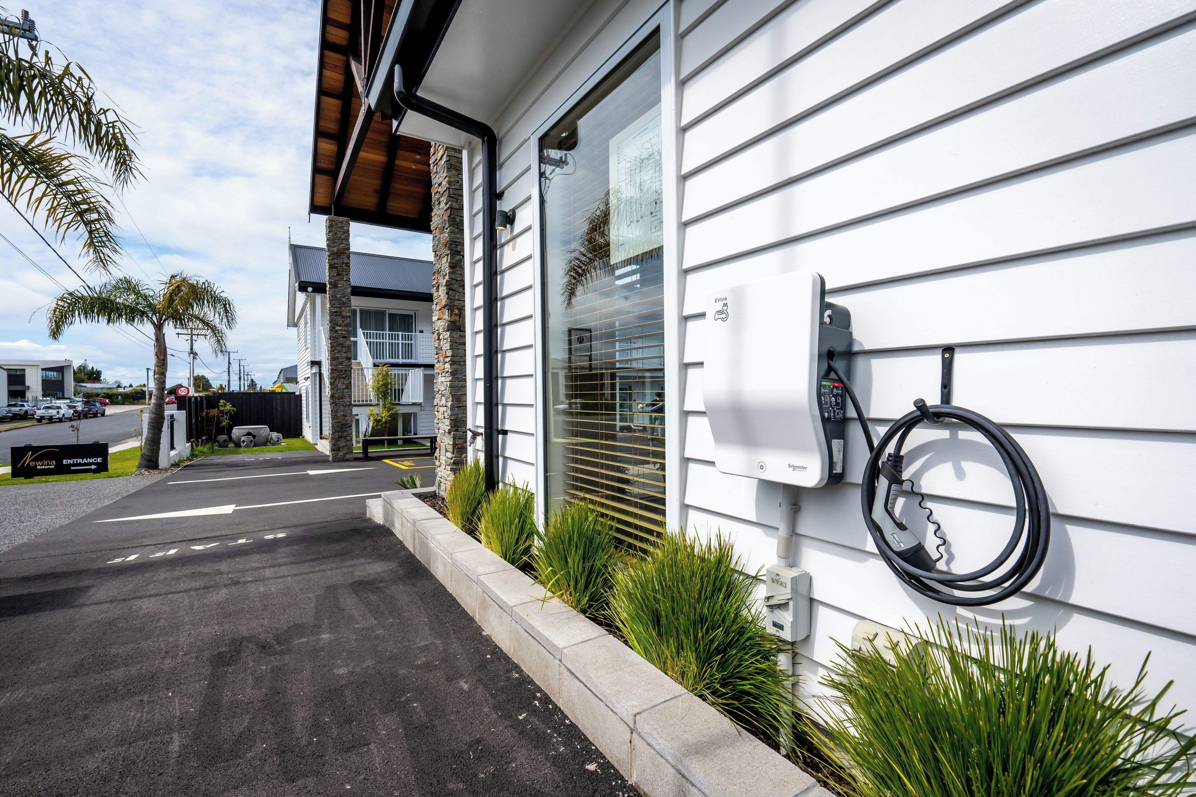 A modern building with a clean entrance, a visible electric vehicle charging station, and a well-maintained garden area.