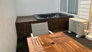 A wooden table with a drain, a hot tub, and an air conditioning unit in a backyard.