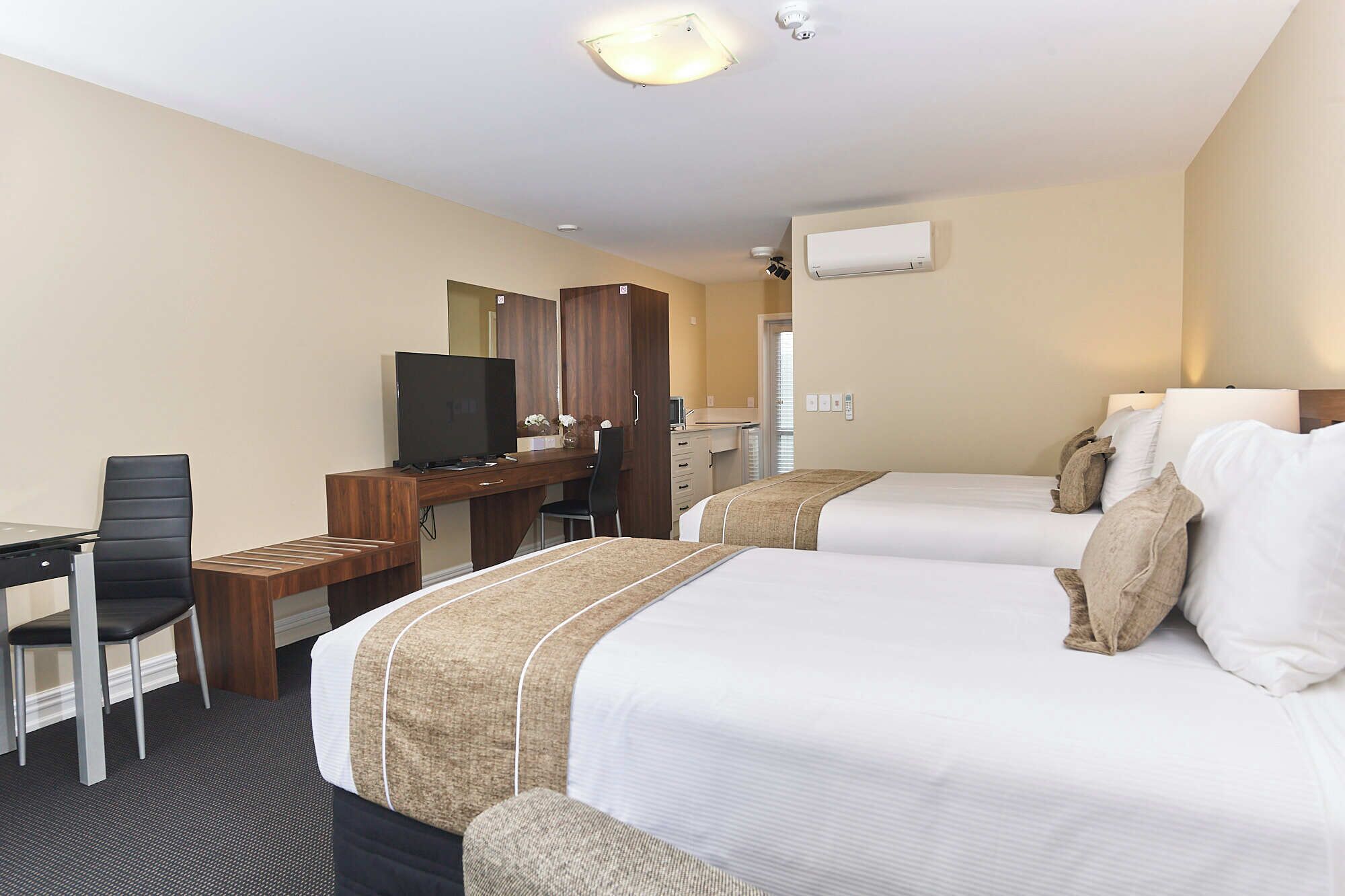 A hotel room with two beds, a desk with a chair, a television, and a wardrobe.