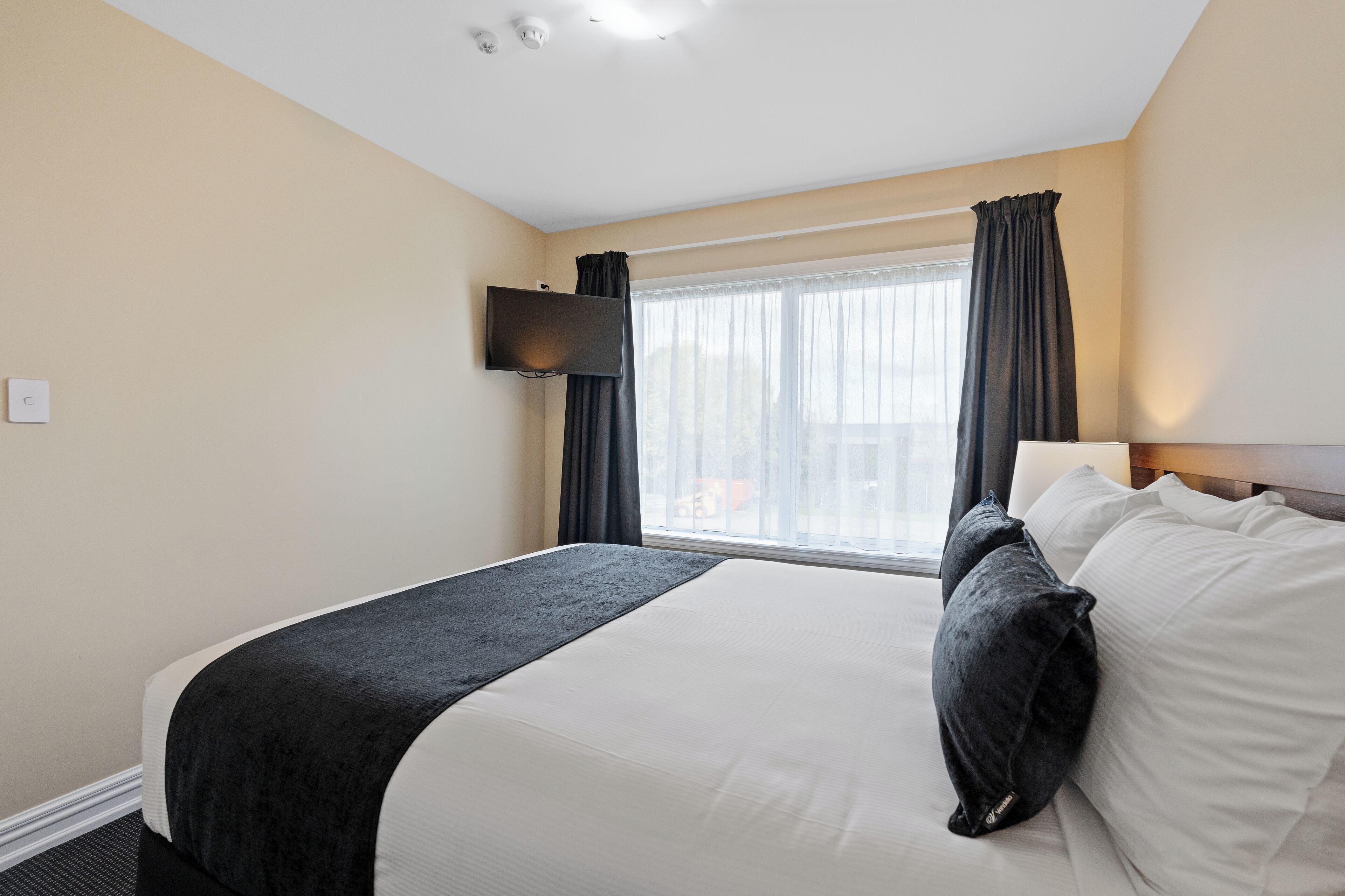 A hotel room with a large bed, a flat-screen TV mounted on the wall, and a window with curtains.
