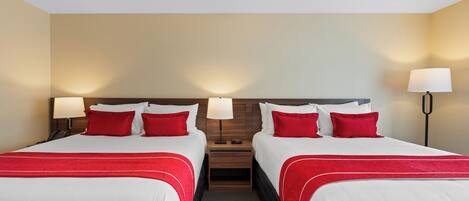 Une chambre d’hôtel avec deux lits, chacun agrémenté de draps blancs et de touches de couleur rouge, une tête de lit en bois, des lampes de chevet et une petite table de chevet.