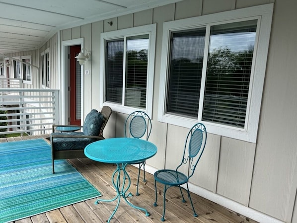 A covered porch with a round table and two chairs, a wooden deck, and a white fence. - Celestial Pointe Condominium 1 Bedroom 1 Bathroom, Sleeps 4 @ Northern Lights (Douglas)